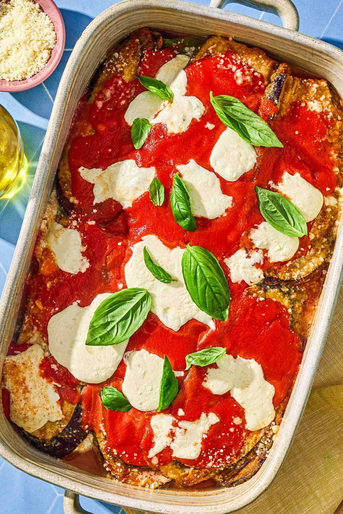 The eggplant parmesan recipe in a baking dish next to a bowl of grated parmesan.