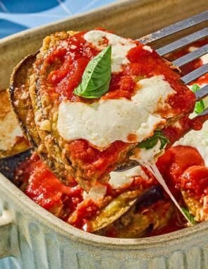 A piece of the eggplant parmesan being lifted from the rest of the casserole in a baking dish.