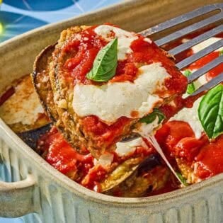 A piece of the eggplant parmesan being lifted from the rest of the casserole in a baking dish.
