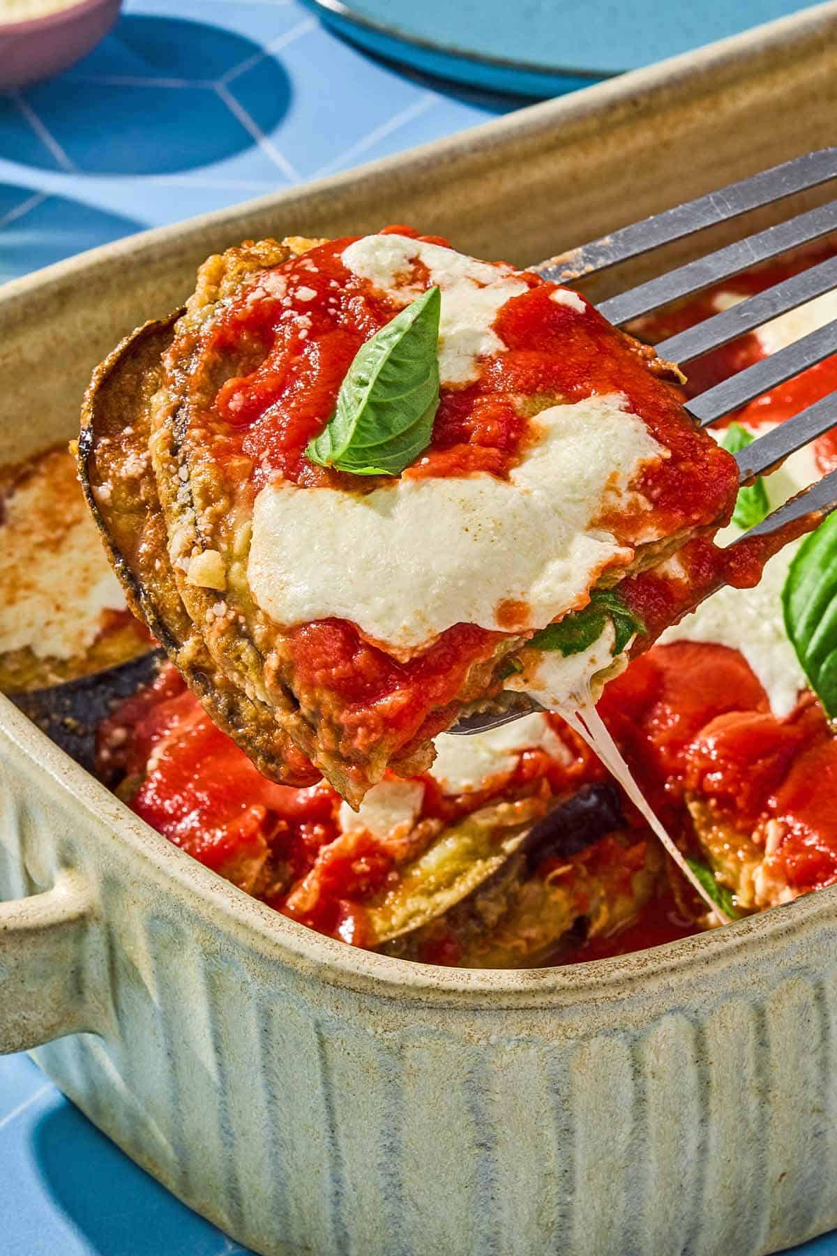 A piece of the eggplant parmesan being lifted from the rest of the casserole in a baking dish.