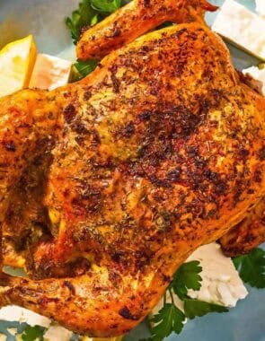 Feta-brined chicken on a platter with parsley, feta, and lemon wedges.