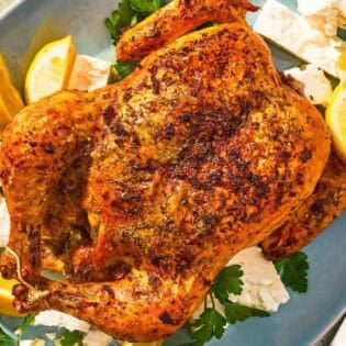 Feta-brined chicken on a platter with parsley, feta, and lemon wedges.