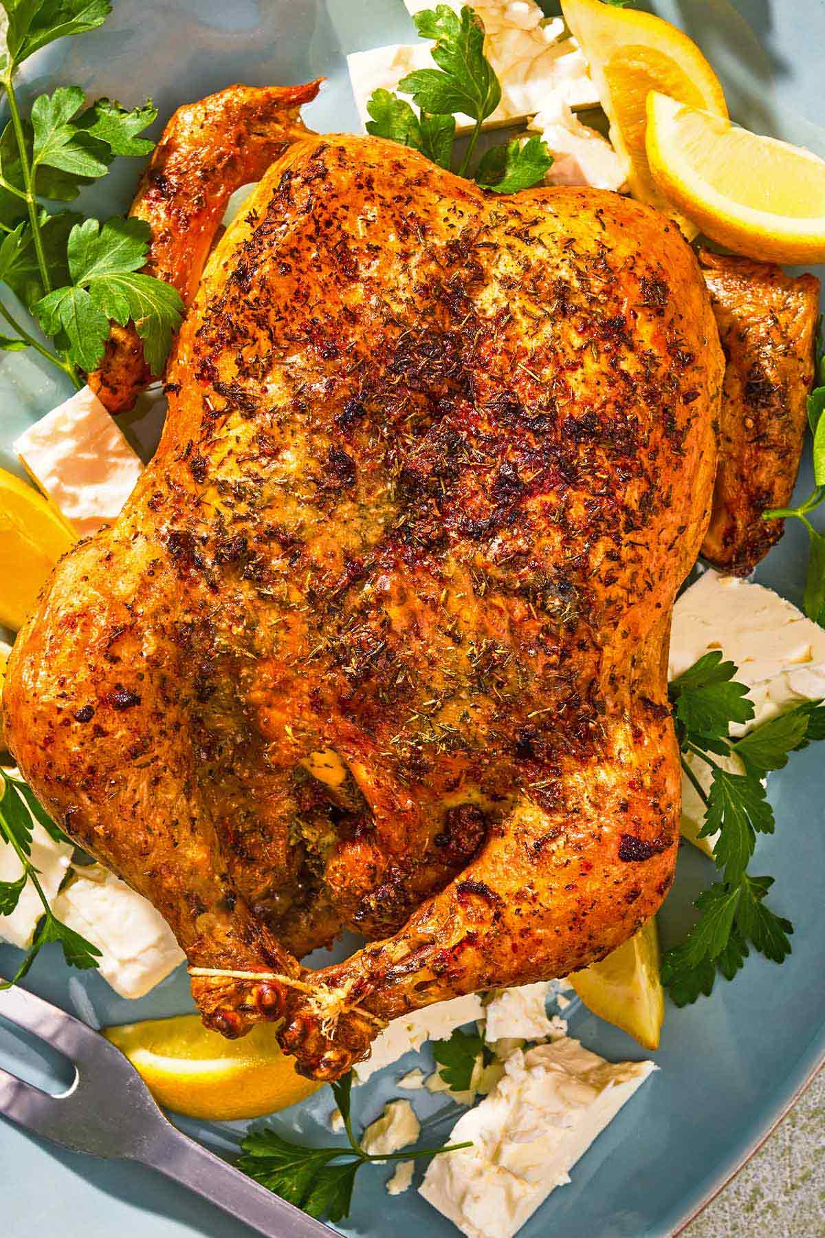 Feta-brined chicken on a platter with parsley, feta, and lemon wedges.