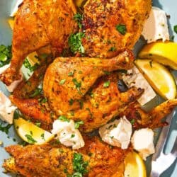 Feta-brined chicken on a platter with feta, lemon wedges and a serving fork.