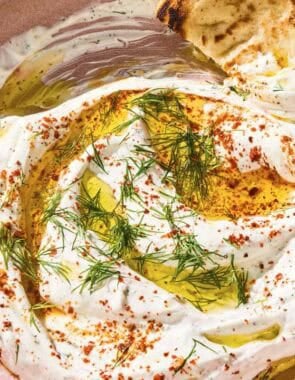Haydari topped with fresh dill, Aleppo pepper and a drizzle of olive oil in a bowl with a pita wedge.
