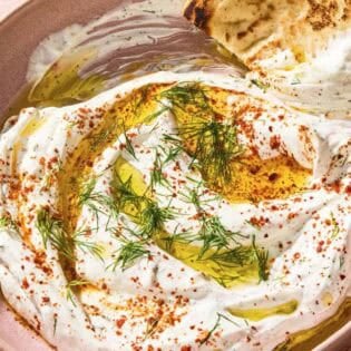 Haydari topped with fresh dill, Aleppo pepper and a drizzle of olive oil in a bowl with a pita wedge.