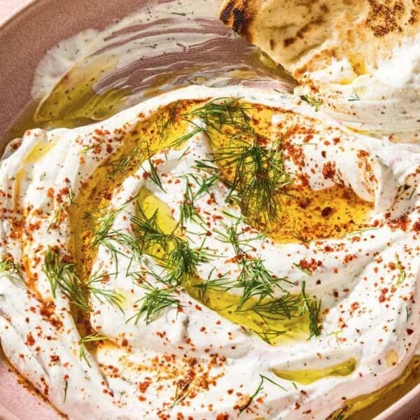 Haydari topped with fresh dill, Aleppo pepper and a drizzle of olive oil in a bowl with a pita wedge.