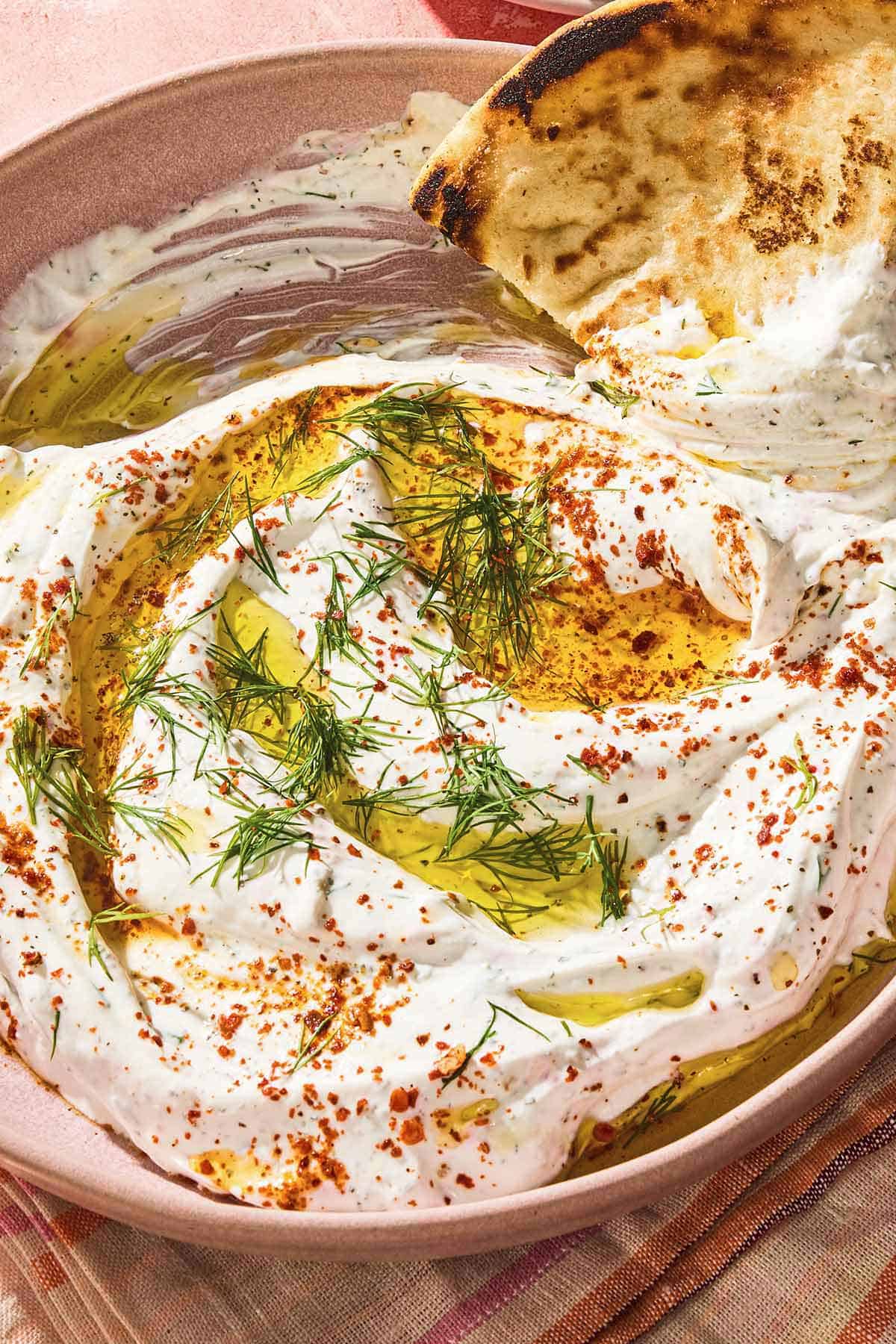 Haydari topped with fresh dill, Aleppo pepper and a drizzle of olive oil in a bowl with a pita wedge.