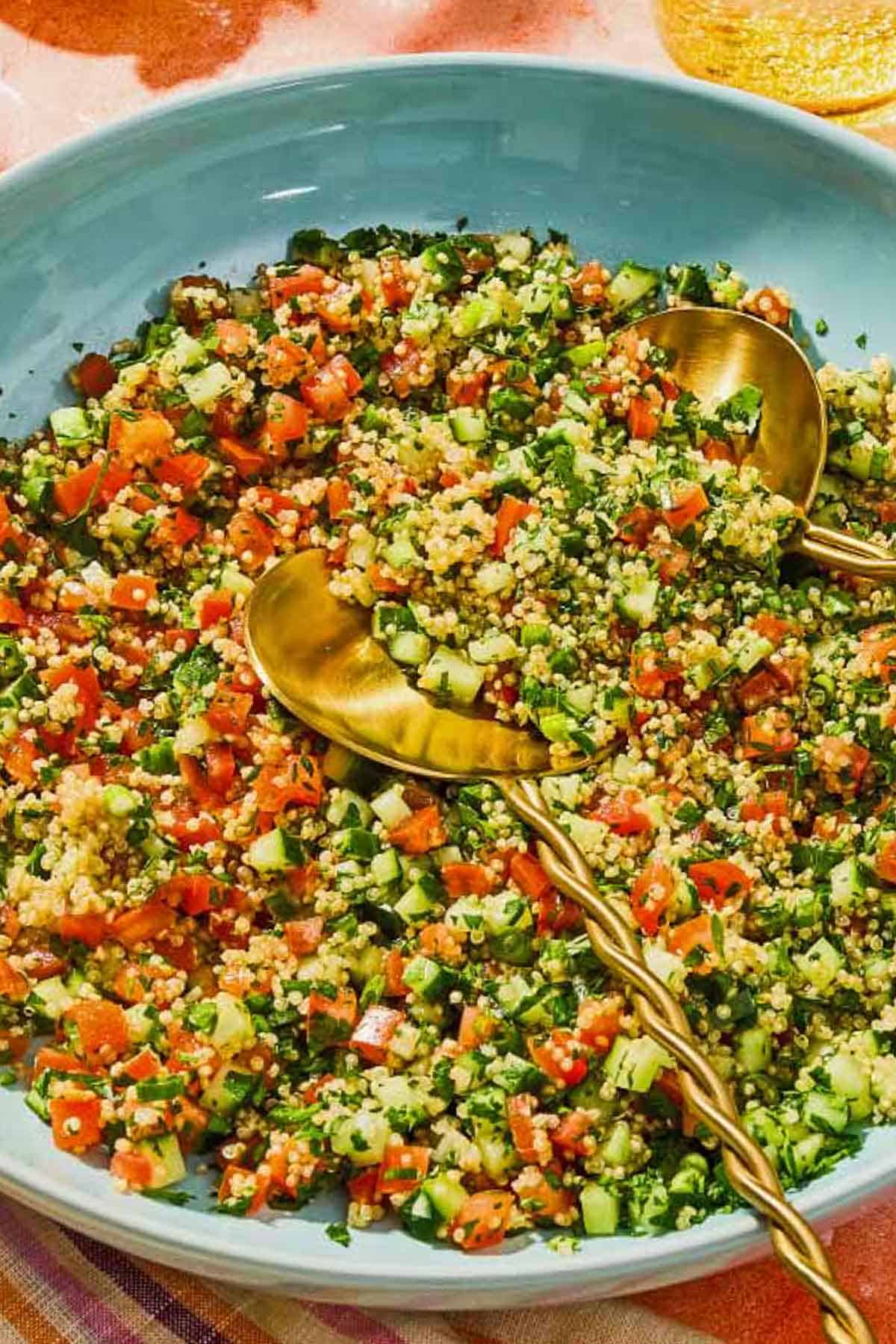 Quinoa tabouli in a serving bowl with serving utensils.