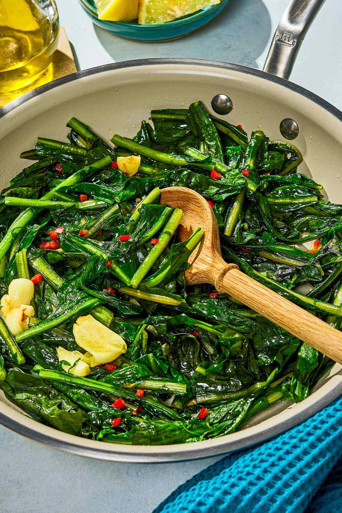 Dandelion greens in a skillet with a wooden spoon.