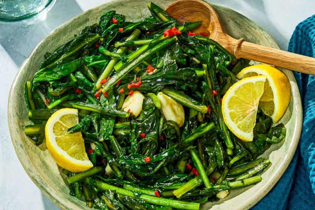 Dandelion greens in a serving bowl with lemon wedges.