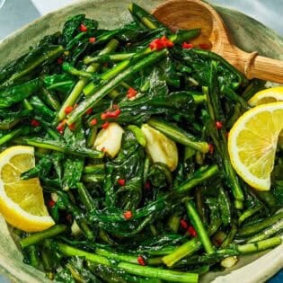Dandelion greens in a serving bowl with lemon wedges.