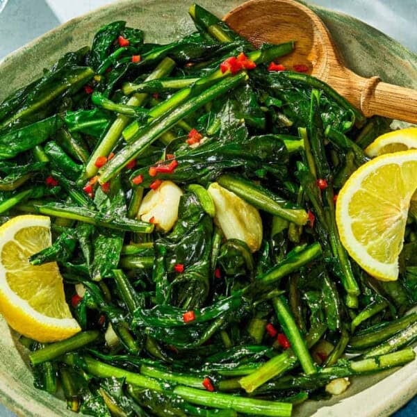 Dandelion greens in a serving bowl with lemon wedges.