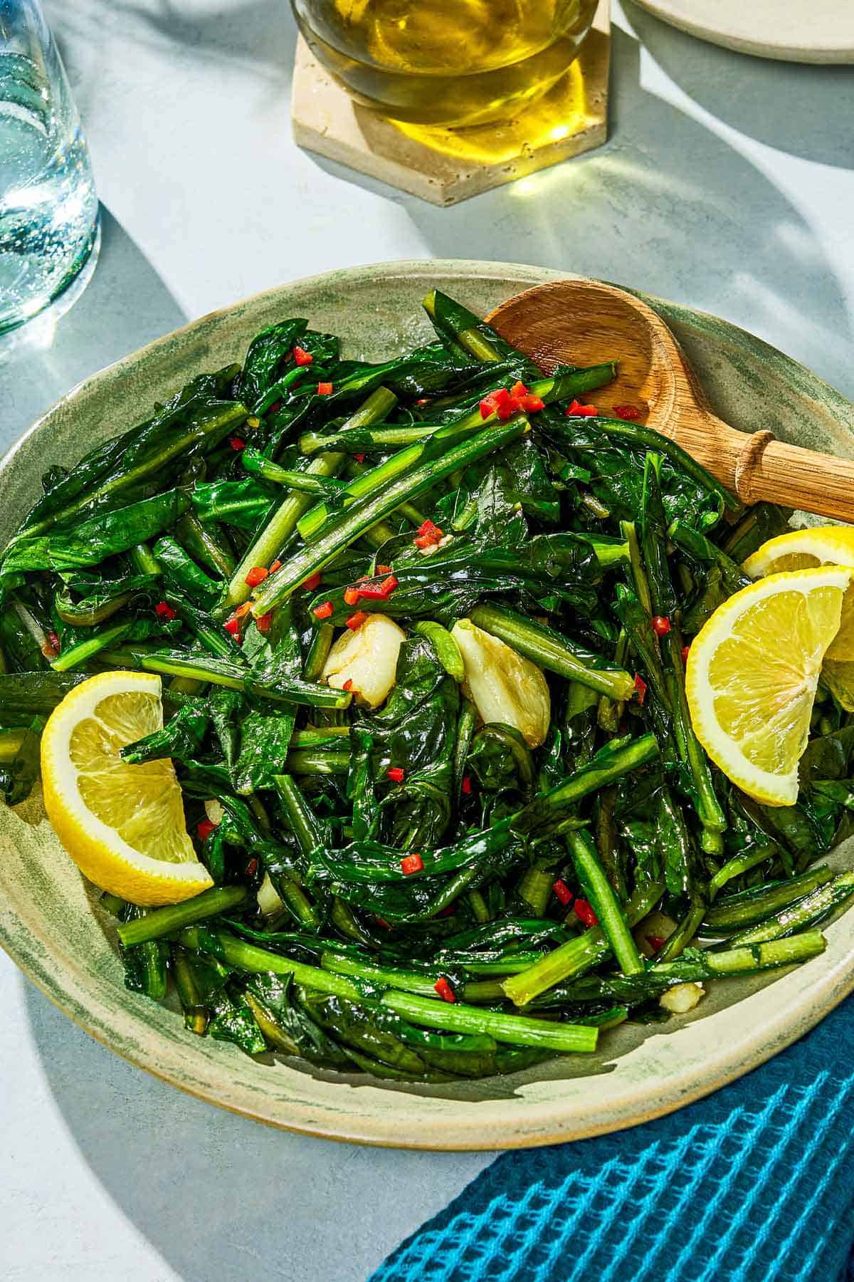 Dandelion greens in a serving bowl with lemon wedges.