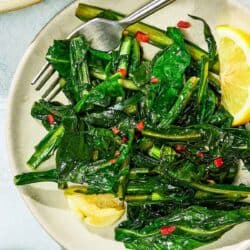Dandelion greens on a plate with lemon wedges and a fork.
