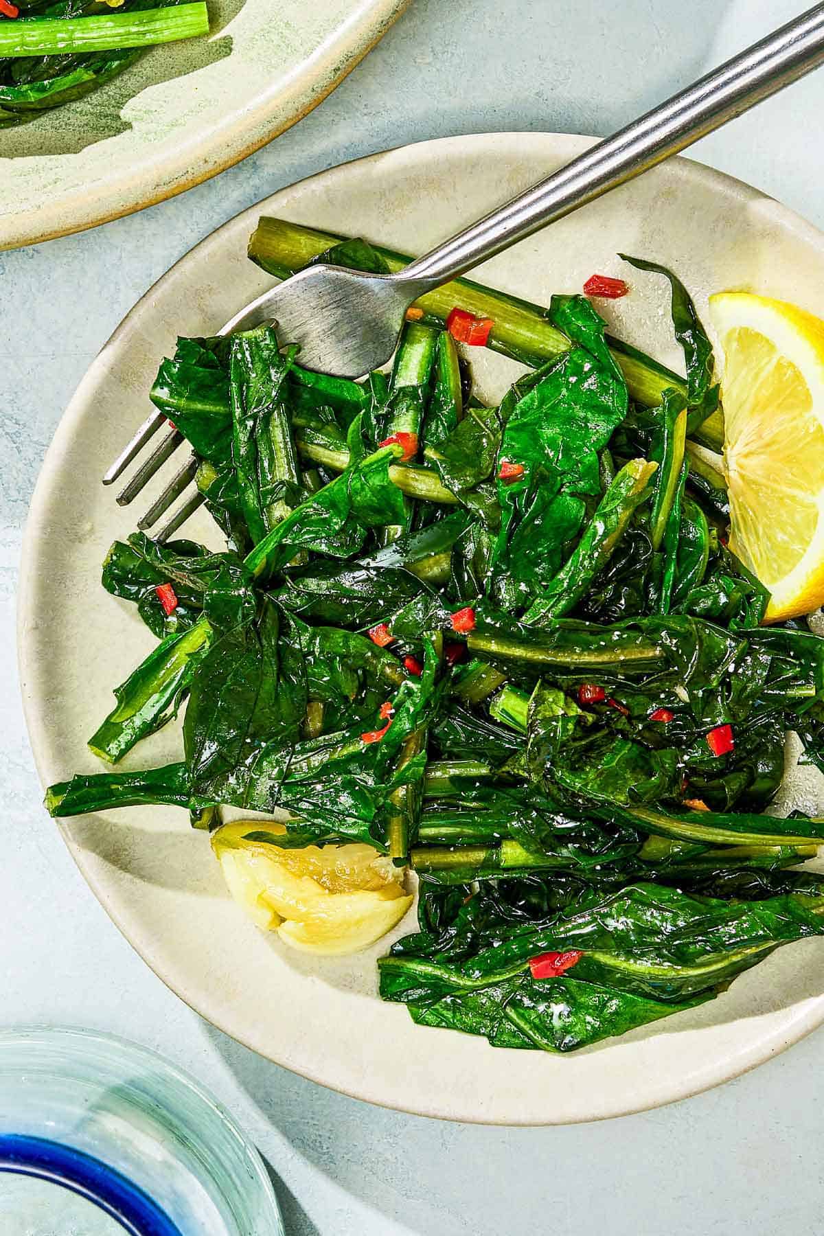 Dandelion greens on a plate with lemon wedges and a fork.