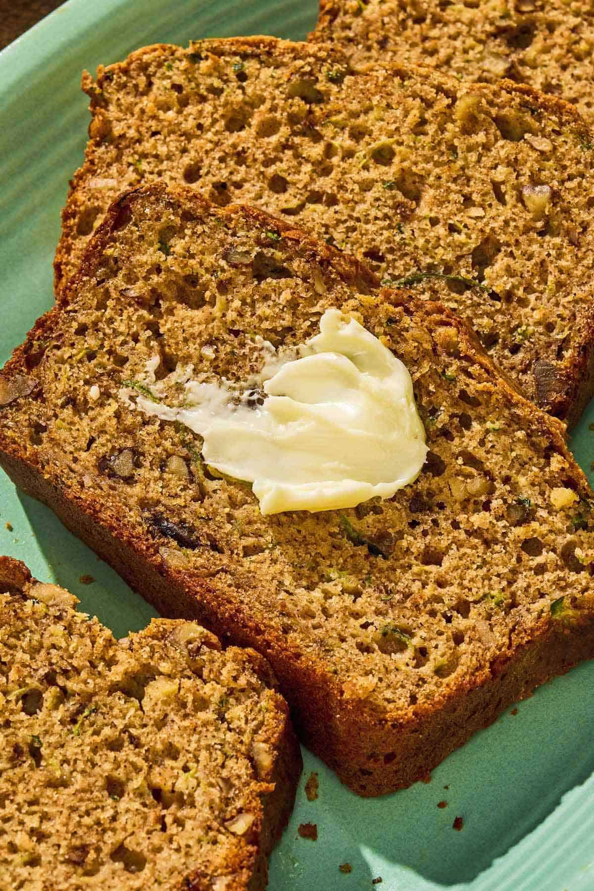 Several slices of zucchini on a platter, one with a dollop of butter.