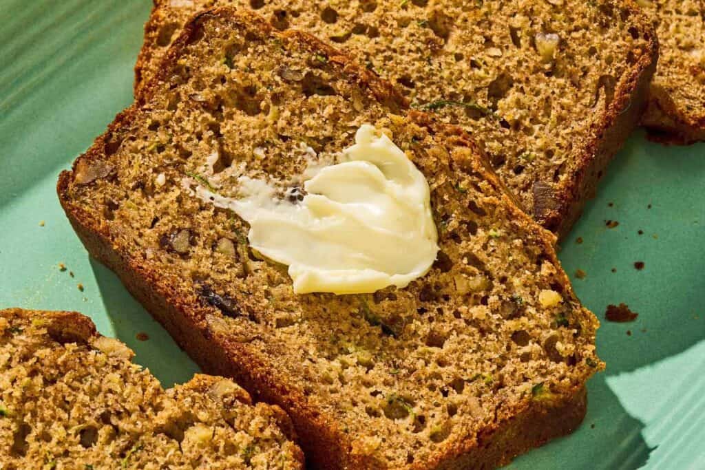 Several slices of zucchini on a platter, one with a dollop of butter.
