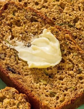 Several slices of zucchini on a platter, one with a dollop of butter.