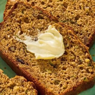 Several slices of zucchini on a platter, one with a dollop of butter.