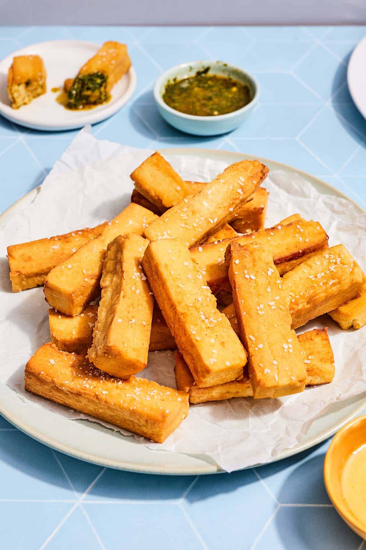 Chickpea panisses on a platter next to a bowl of chermoula and a plate with two chermoula halves.