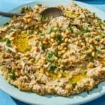 Baba ganoush in a bowl with a spoon next to a a plate of vegetables.