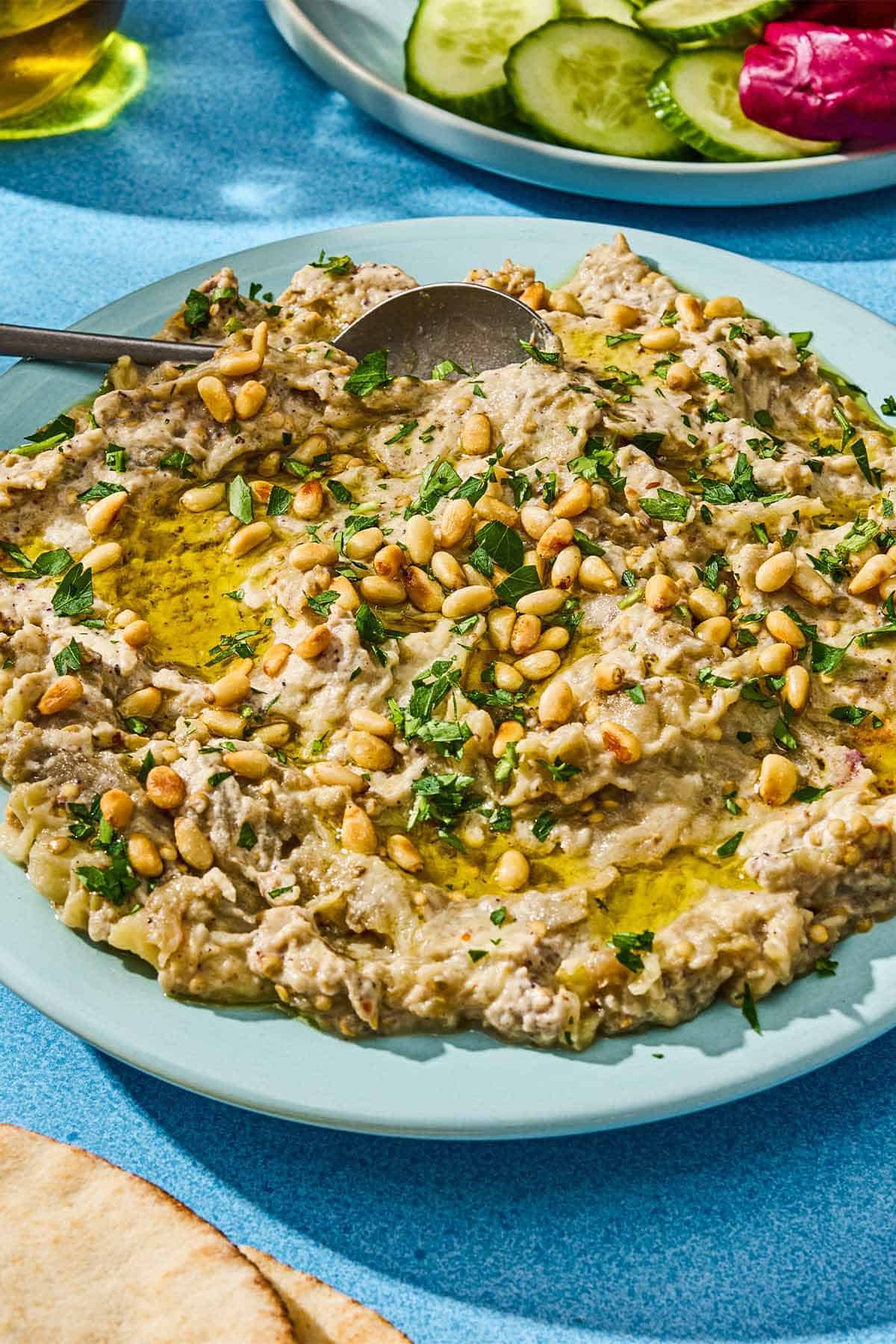 Baba ganoush in a bowl with a spoon next to a a plate of vegetables.