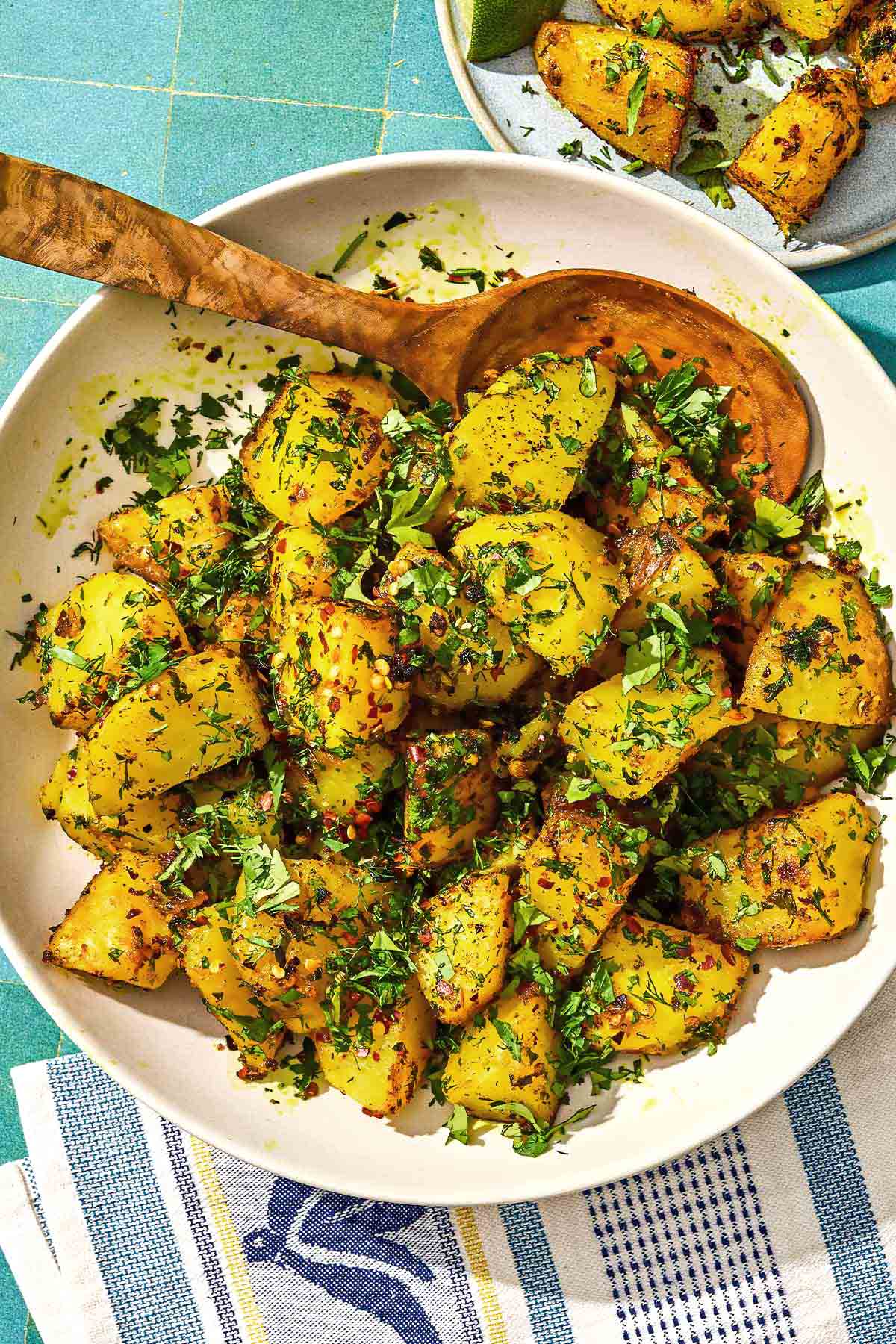 Batata Harra dans un bol de service avec une cuillère à côté d'une portion de la recette sur une assiette.