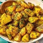 Batata Harra dans un bol de service avec une cuillère. À côté se trouve une assiette avec des quartiers de citron vert et un bol de flocons de piment rouge.