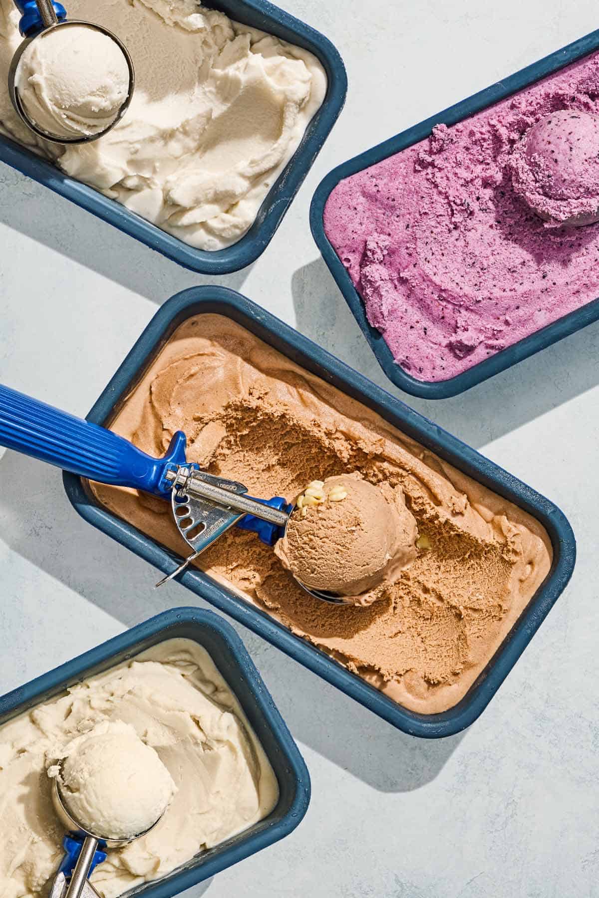Four containers of dairy free ice cream with scoops: vanilla, tahini, blueberry, and chocolate hazelnut.
