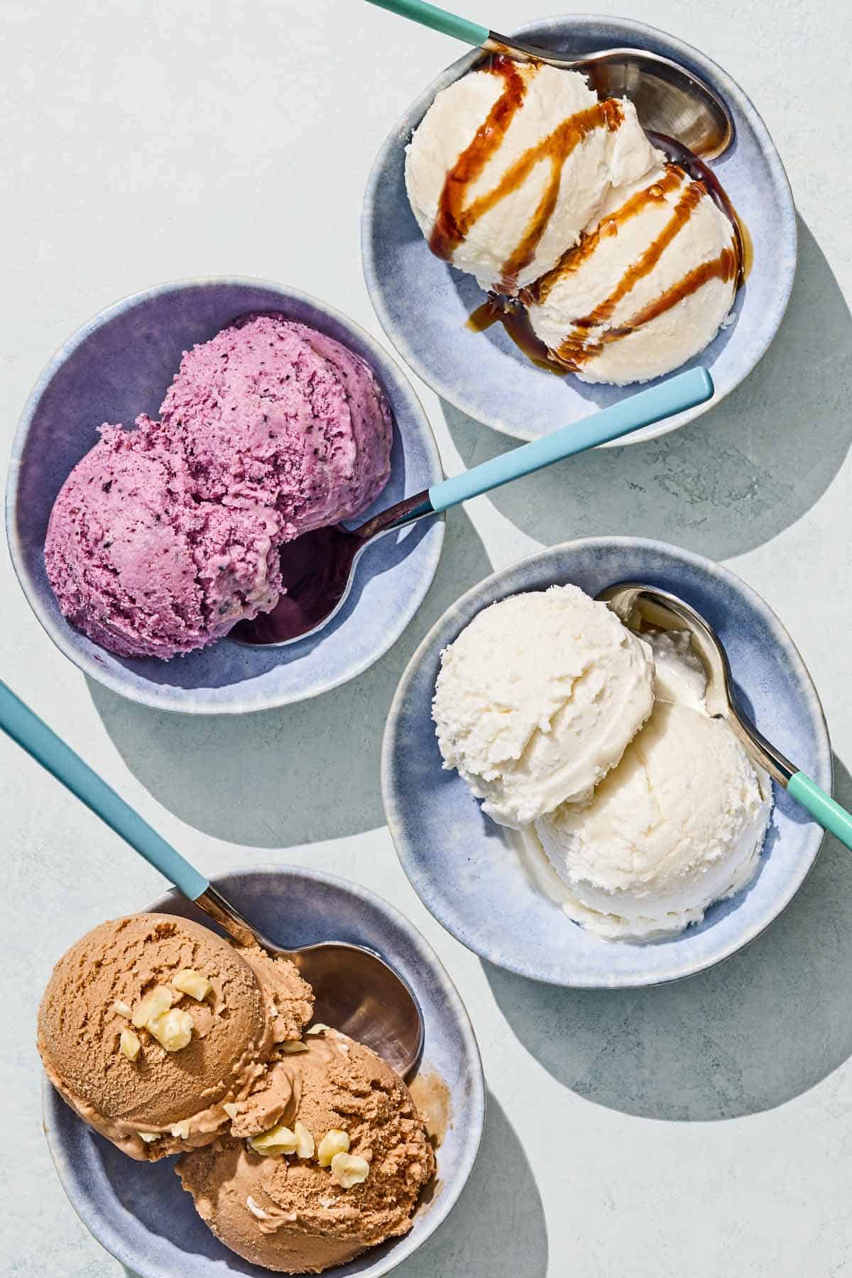 Bowls of tahini, blueberry, vanilla and chocolate hazelnut dairy free ice cream with spoons.