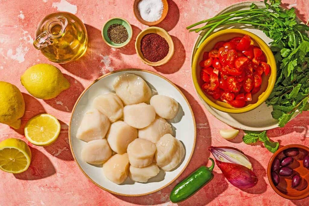 Інгрэдыенты для грабеньчыкаў, прыгатаваных на грылі, у тым ліку грабеньчыкі, соль, перац, лімоны, аліўкавы алей, памідоры черрі, лук-шалот, часнык, пятрушка, мята, аліўкі каламата, халапеньё і сумах.