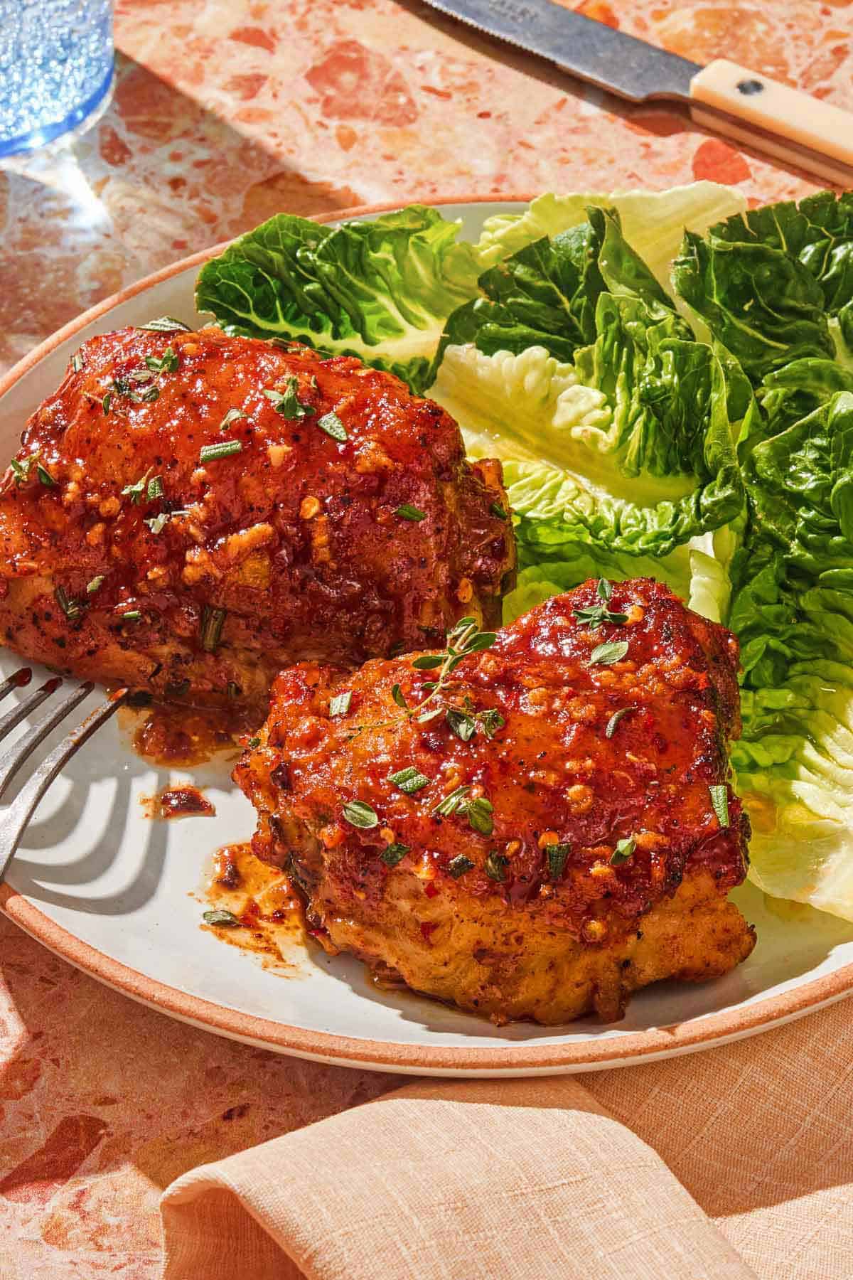 A plate with two honey mustard chicken thighs, a salad and a fork.