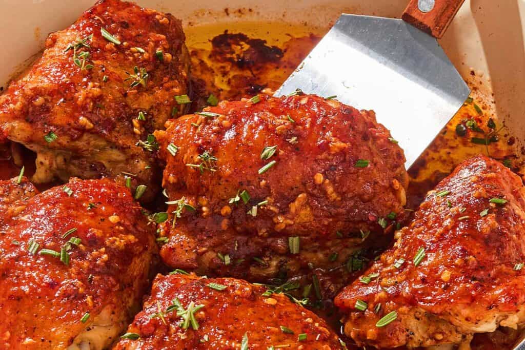 The honey mustard chicken thighs in a skillet with a spatula.