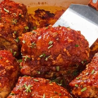 The honey mustard chicken thighs in a skillet with a spatula.