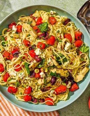 The Mediterranean pasta in a serving bowl next to serving utensils and bowls of feta and red pepper flakes.