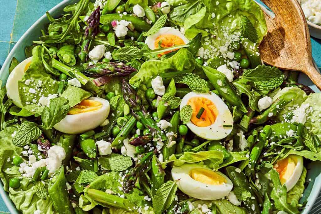 A spring green salad in a serving bowl with a serving spoon.