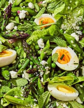 A spring green salad in a serving bowl with a serving spoon.