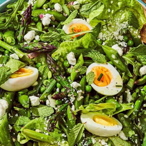 A spring green salad in a serving bowl with a serving spoon.