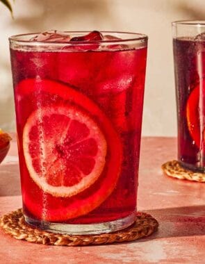 Two glasses of tinto de verano on coasters next to a bowl of sliced lemon and oranges.