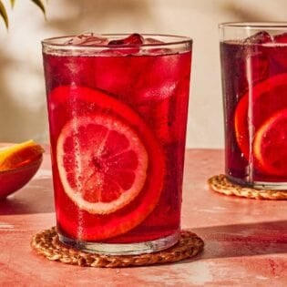 Two glasses of tinto de verano on coasters next to a bowl of sliced lemon and oranges.