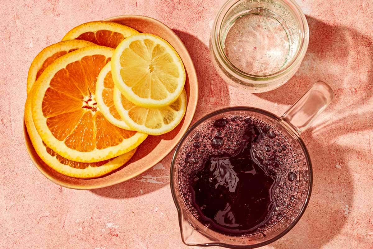 Ingredients for tinto de verano including red wine, lemon lime soda, and orange and lemon slices.