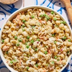 Tuna pasta salad in a serving bowl next to a bowl of salt and wooden serving utensils.