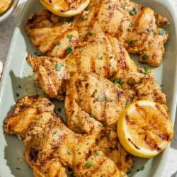 Several lemon chicken thighs on a platter with grilled lemon halves.