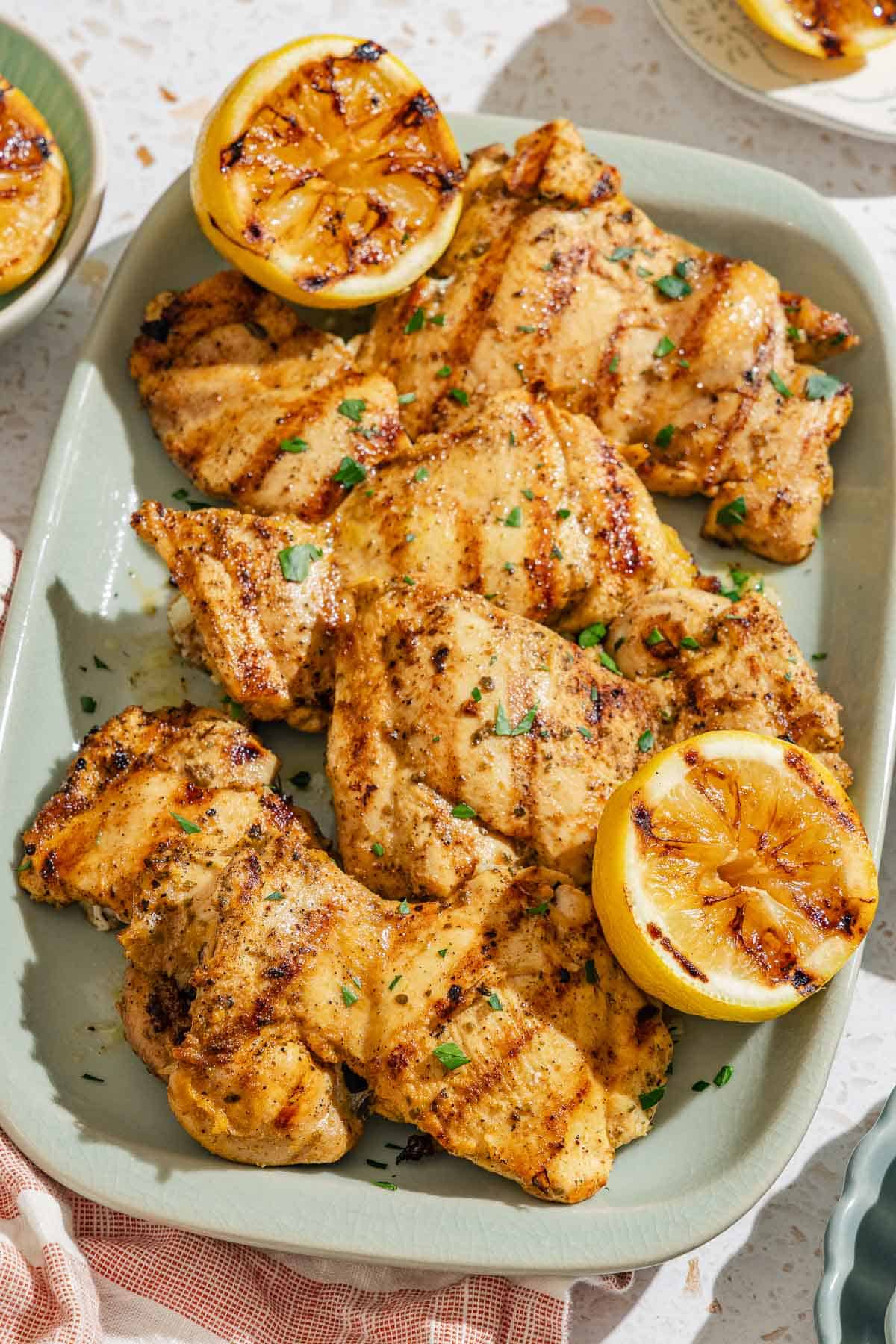 Several lemon chicken thighs on a platter with grilled lemon halves.