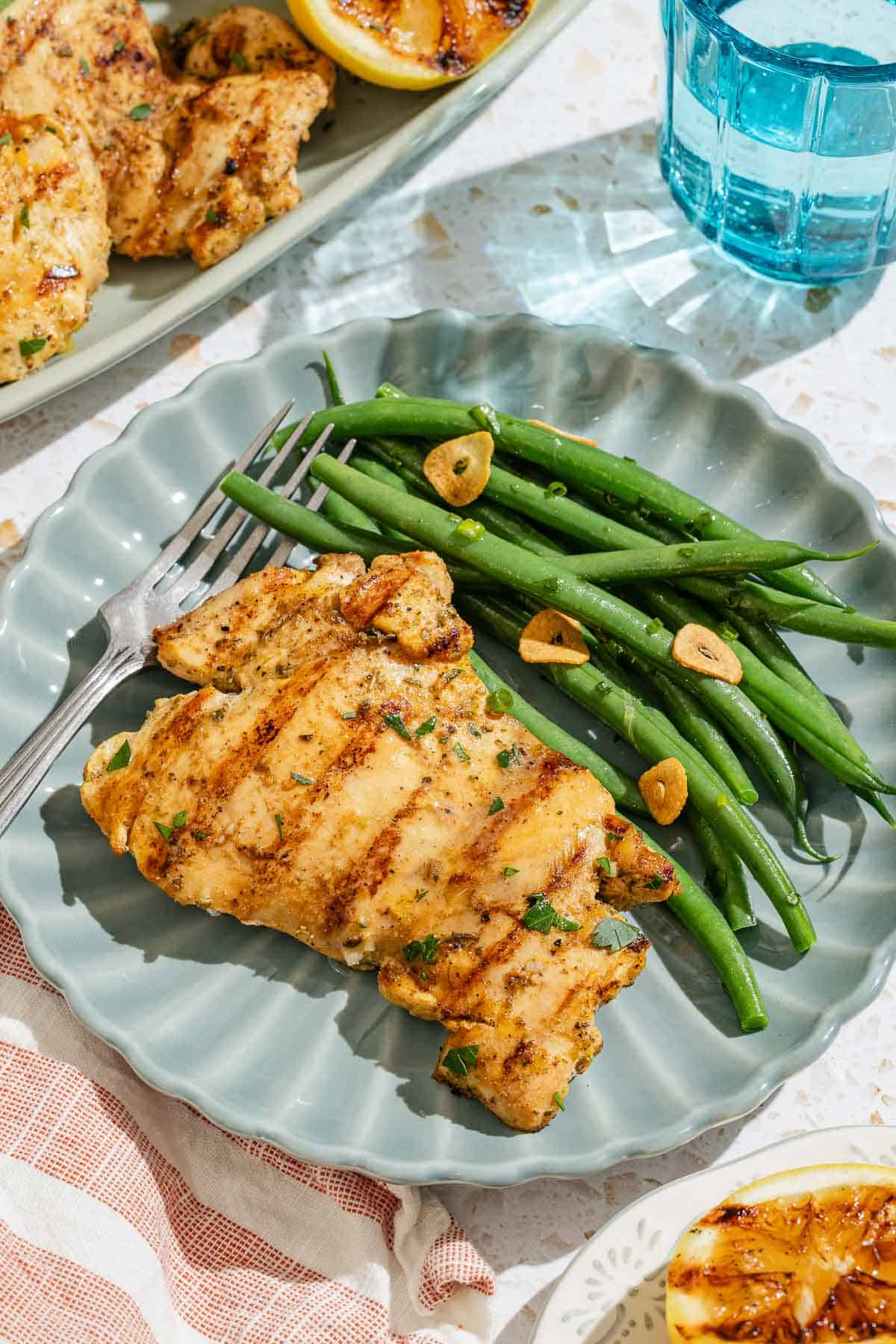 A serving of lemon chicken on a plate with green beans and a fork.