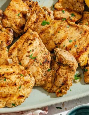 Several lemon chicken thighs on a platter with grilled lemon halves.