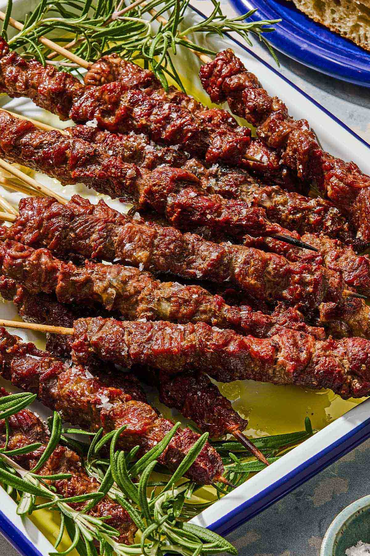 Several arrosticini skewers on a platter with sprigs of rosemary.