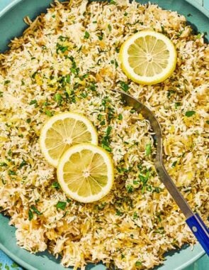 Greek lemon rice topped with lemon wheels in a bowl with a serving spoon.
