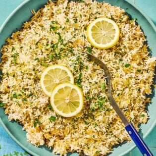 Greek lemon rice topped with lemon wheels in a bowl with a serving spoon.